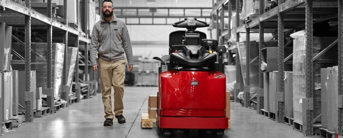 Image of Raymond Forklift equipped with Advance Operator Assist Technology with operator walking parallel to the truck in a warehouse. 